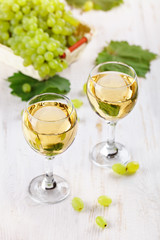 Glasses with white wine and fresh grapes on a wooden table.