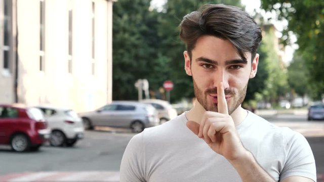 Handsome man making a shushing gesture raising his finger to his lips in a seductive gesture as he asks for silence, with a smile
