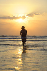 Silhouette of young beautiful and sexy asian woman running free and happy having fun at sunset beach in Bali