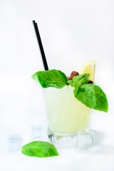 front view of cold fresh tropical cocktail in whiskey glass decorated with a slice of lemon, mint, ice cubes, straws and hazelnut on light background