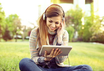 Smiling woman listening to music with tablet and headphones sitting outdoors in a city park