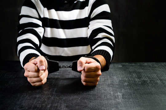 unidentified prisoner in handcuffs in prison stripped uniform sitting on the chair in the dark interrogation room. The interrogation of the arrested