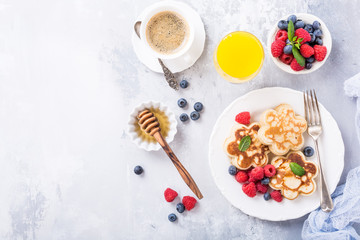 Flat lay with breakfast with scotch pancakes in flower form, berries and honey on light wooden table. Healthy food concept with copy space.