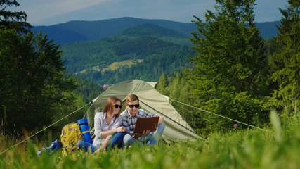 Couple of tourists using laptops in the camping. Against the background of the picturesque mountains