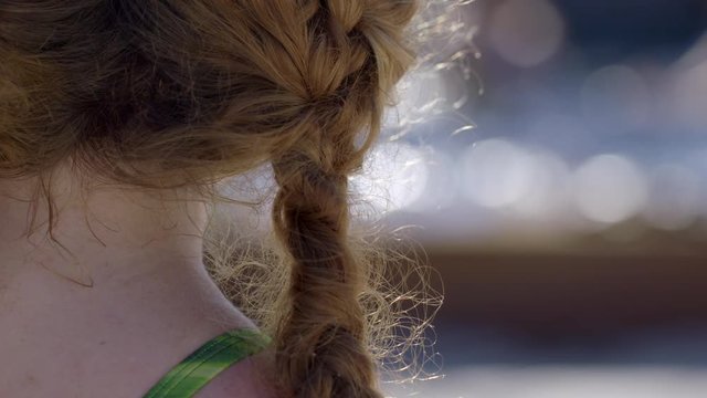 Over the shoulder view of red-haired young woman look at swimming pool in soft focus distance. Slow motion 4K recorded at 60fps