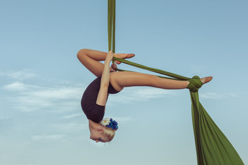 Woman air gymnast performs a trick on a hammock high in the sky.