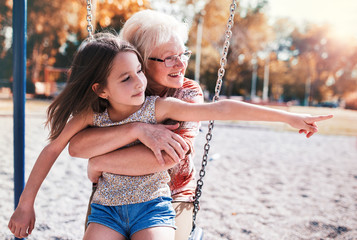 Cute little girl and her grandmother having fun on the playground in the park