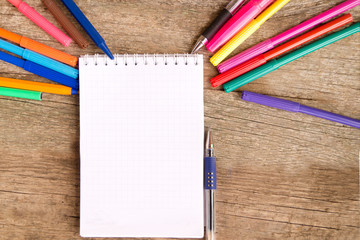 Open white notepad with colorful felt-tip pens and ball pens on the wooden table