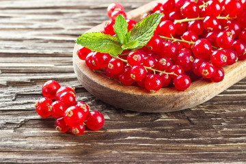Ripe redcurrants in a wooden plate on a rustic wooden background.