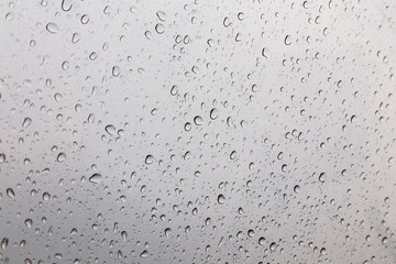Rain drops on window glasses surface with gray sky background .Rain pattern close up of raindrops isolated on gray background.