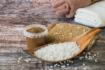  Beauty and hygiene. Body care. Sea salt, a round jar with cleansing scrub, a sponge made from natural material and terry towels on a wooden background.