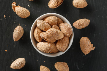 Almond in shell in a white bowl on a black wooden table, top view