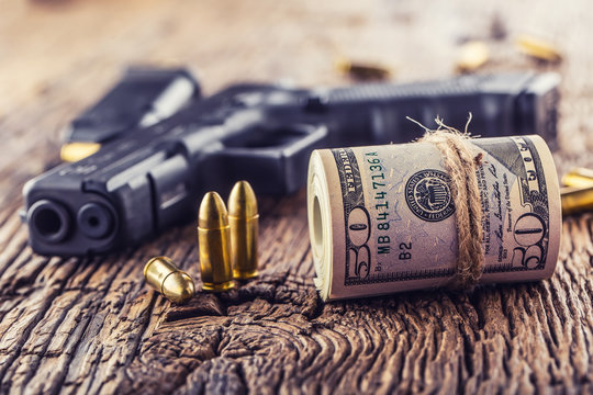 Gun and money. 9 mm pistol gun bullets strewn and roll dollar banknotes on rustic oak table
