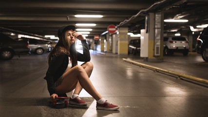 Fototapeta na wymiar Beautiful young woman with skateboard posing at underground parking garage