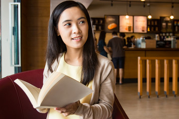 Asian woman reading book inside coffee shop