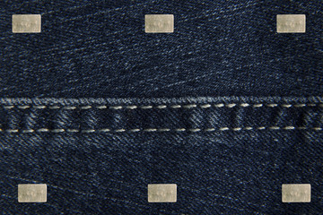 Denim blue fabric with small rectangular metal label for your text. The texture is a close-up macro shot.