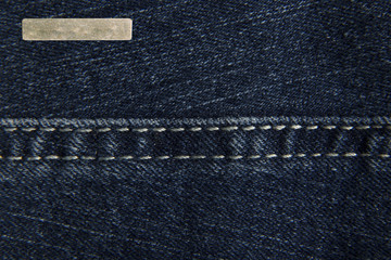 Denim blue fabric with one small rectangular metal label for your text. The texture is a close-up macro shot.