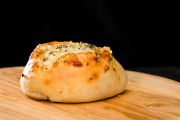 close-up of homemade mini pizza bun topped with cheese, garlic and herbs on round wooden board on dark background