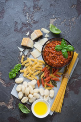 Freshly made bolognese sauce with different types of raw pasta, parmesan, fresh green basil and olive oil, top view, vertical shot