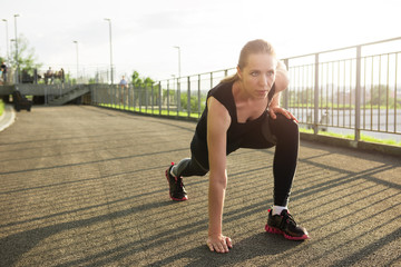 A woman in sportswear doing fitness exercises. City in sunny evening.