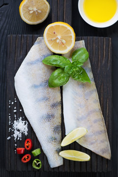 Above view of fresh uncooked sudak fish and condiments on a black wooden chopping board, closeup
