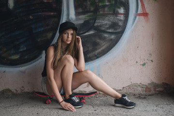 Beautiful young woman with skateboard posing near wall with graffiti