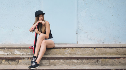 Beautiful young woman with skateboard sitting on concrete stairs outdoors
