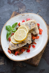 Fried sudak with sauteed vegetables served on a white plate, brown stone background, studio shot