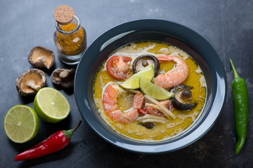 Thai green curry soup with addition of shrimps and shiitake served in a dark gray plate, studio shot
