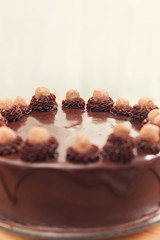 Frosted chocolate cake with decorative swirls and truffles on a wood table.