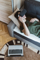Beautiful young woman lying on the bed and enjoying virtual reality at her home.