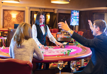 Cute lady casino dealer at poker table. Happy couple is playing Black Jack.