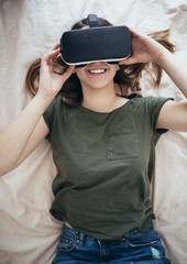 Beautiful young woman lying on the bed and enjoying virtual reality at her home.