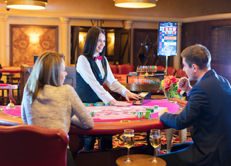 Cute lady casino dealer at poker table. Happy couple is playing Black Jack.