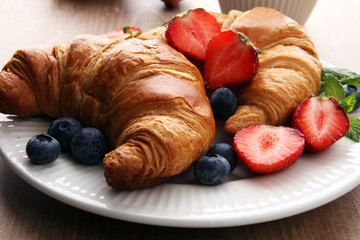 Delicious breakfast with fresh croissants, coffee and ripe berries on old wooden background