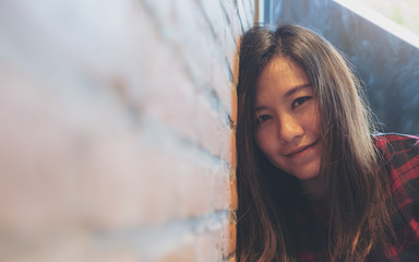 Closeup image of a smiley beautiful Asian woman leaning on brick wall in modern cafe