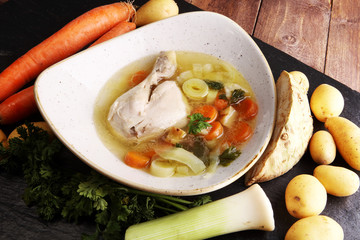 Bone broth made from chicken with carrots, onions various fresh vegetables in a pot - colorful fresh clear spring soup. Rural kitchen scenery bouillon or stock