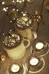 Ceramic stylish cups in sweaters and christmas retro garland on bokeh lights background. Shallow depth of field. Tinted photo