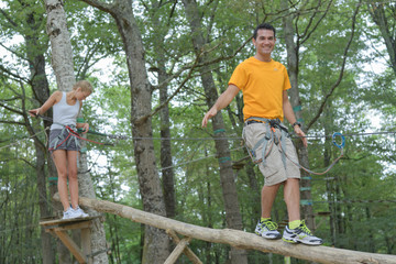 Naklejka na ściany i meble couple walking on suspended trunk at the adventure park