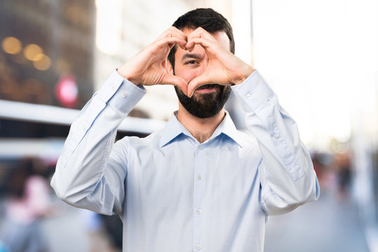 Handsome man with beard making a heart with his hands on unfocused background