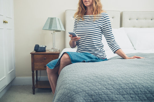 Woman on bed in hotel room using smart phone