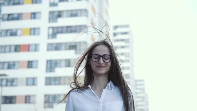 A cute girl is standing on a city background, in business clothes. Hair moves from the wind. Feels free and enjoyable slow mo