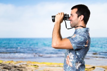 Handsome man with flower shirt with binoculars at the beach