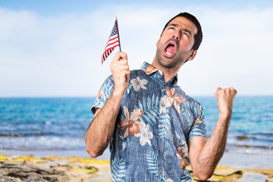 Handsome man with flower shirt holding an american flag at the beach
