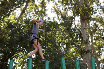 Fit, sporty woman enjoying in a climbing adventure high wire park between trees. Challenge, success, breaking fear concept.