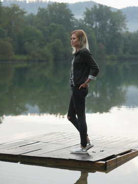 Young blonde woman on wooden pallet of water with hands in pocke