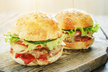 delicious burgers with meat,  cheese, tomato and salad on wood cutting board in sunlight 