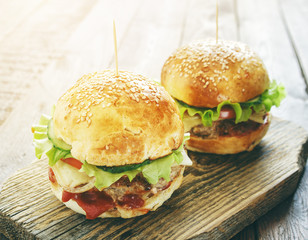 two homemade burgers with green salad leaf, cheese and beef on old rustic wood cutting board in sunlight 