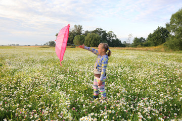 Śliczna dziewczynka bawi się parasolką wśród polnych kwiatów.