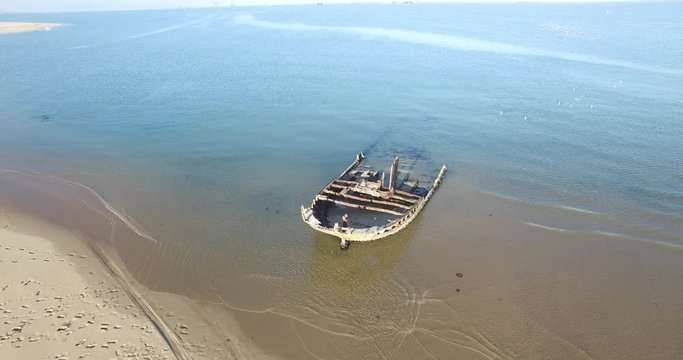 Aerial view drone video of Pelican Point Lodge and Paratus lighthouse on sand beach peninsula, shipwreck and lagoon with ocean background with ships at Namibia's Atlantic west coast